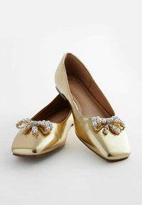 Ballerines dorées avec une finition brillante, ornées d'un nœud décoré de perles et de strass sur la zone des orteils.