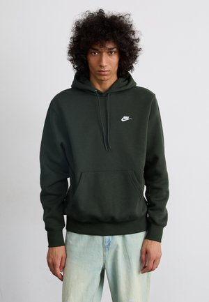 Hoodie de algodão verde com um bolso frontal e capuz com cordão; apresenta um pequeno logótipo branco da Nike no peito. Usado com jeans azul claro.