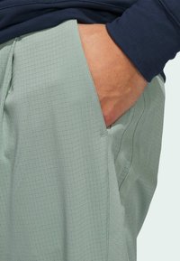 Light green, textured pants with a grid pattern, featuring a side pocket. A navy sleeve is visible above, bringing contrast to the look.
