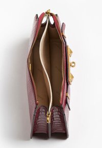 Bolso rectangular burdeos con textura de cocodrilo, que cuenta con dos compartimentos, cremalleras doradas y acentos metálicos en los lados.