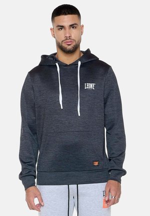 Mann trägt dunkelgrauen Hoodie mit weißen Kordeln und "LEONE 1947"-Logo, kombiniert mit hellgrauen Jogginghosen.