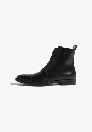 Bottine en cuir noir avec un bout arrondi, laçage à l'avant, tirette à l'arrière et des détails de couture subtils le long de la semelle.