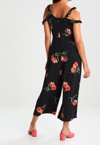 Czarny kwiatowy kombinezon z odkrytymi ramionami i falbaniastymi ramiączkami, w kropeczki, oraz szerokimi, ściąganymi nogawkami. Zestawiony z różowymi butami na słupku.