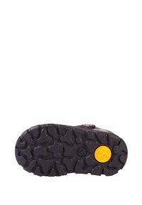 Suela de zapato de goma con un patrón de textura en negro, que presenta un acento circular amarillo y pequeñas estrías en ángulo para mayor agarre.