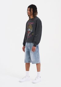 Felpa nera con grafica di una tigre, abbinata a pantaloni corti di jeans azzurri. Indossata con sneakers bianche e calzini alla caviglia.