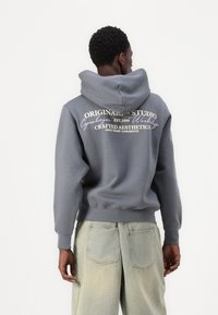 Grijze hoodie met witte tekstgraphics op de achterkant, gecombineerd met lichtgekleurde, wijduitlopende jeans. Zachte, gestructureerde stof.