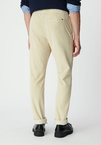 Pantalones de pana beige con una superficie texturizada, corte ajustado y dobladillos enrollados. Presentan un bolsillo trasero y un sutil detalle de marca.