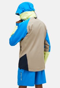 Bunte wasserdichte Jacke mit einer Mischung aus Blau, Beige und Neon-Gelb; ausgestattet mit einer Kapuze und Taschen für praktische Nutzung.