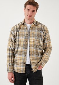 Geel en zwart geruite flanellen shirt met een button-down kraag en lange mouwen, met een zachte textuur en contrasterende witte accenten.