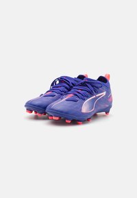 Des chaussures de football violettes avec des accents roses, une tige texturée et un design à lacets. Elles présentent des crampons visibles sur la semelle pour une meilleure adhérence.