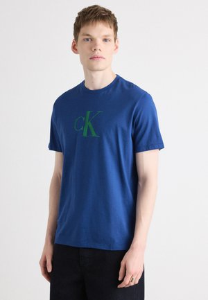 Blue cotton t-shirt featuring a large green logo "cK" on the front. Classic crew neck design and short sleeves. Smooth texture.