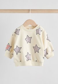 Pull-over jaune avec un motif d'étoiles, comprenant des étoiles grises bordées de noir. Matière légère, col et poignets côtelés, et pressions sur les côtés.