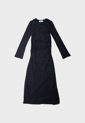 Černé šaty s dlouhým rukávem a přiléhavým střihem, zdobené texturovaným vzorem puntíků, na bocích s nařasením a kulatým výstřihem.