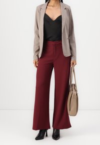 Beige blazer över en svart cami, kombinerad med vida bourgogne-byxor och svarta högklackade skor. En ljusbrun handväska fulländar looken.