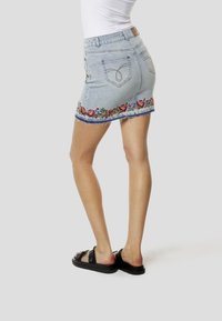 Jupe mini en denim bleu clair avec broderie florale à l'ourlet. Caractéristiques : bords effilochés et design traditionnel à cinq poches.