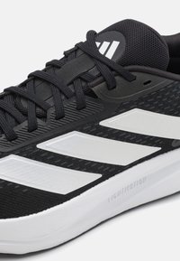Chaussure de sport noire avec des rayures blanches, lacets noirs, upper en mesh et semelle blanche rembourrée portant l'étiquette "LIGHTMOTION."