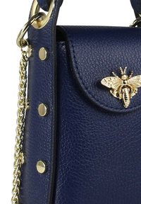 Marineblauwe leren handtas met gestructureerd oppervlak, hardware in goudkleur, afneembare kettingriem en een metalen bijfiguur op de klep.