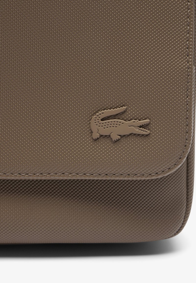 Sac à main marron texturé avec un fermoir rabat, arborant un logo crocodile subtil dans une teinte plus foncée, mettant en valeur son matériau et son savoir-faire.