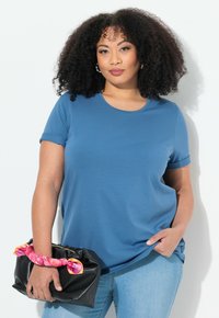 Modrá krátká tričko s krátkým rukávem z měkké tkaniny, kulatým výstřihem, v kombinaci s černou kabelkou s barevným vzorovaným držadlem.