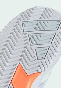 Kengän ulkopohja on valkoista kumia, jossa on herringbone-kuvio. Ominaisuuksiin kuuluu vaaleanharmaa sävyinen teksturoitu kolmiomalli ja orange korostus.