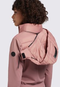 Rosa, gepolsterte Jacke mit hohem Kragen und abnehmbarer Kapuze. Verfügt über ein schwarzes Logo-Patch und einen verstellbaren Kordelzug an der Kapuze. Glatte Textur.
