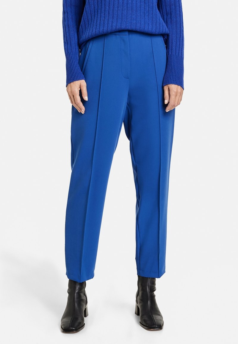 Blå skräddarsydda byxor med en slät textur, utrustade med frontveck och en avslappnad passform. Kombineras med svarta anklarstövlar.