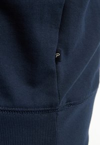 Tmavě námořnická modrá tkanina s texturovaným povrchem, která má viditelné švy a malou černou etiketu s bílým textem po straně.