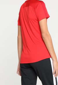 Camiseta atlética roja de manga corta con detalle en la parte trasera de malla, combinada con pantalones negros con rayas blancas en los laterales.