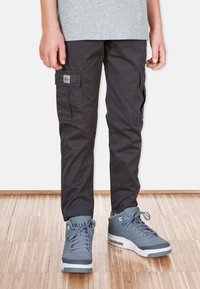 Svarts cargo-byxor med sidofickor och en liten logotyp, i kombination med gråa sportskor med strukturerad ovandel och vita sulor.