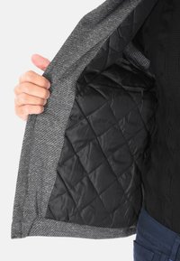 Giacca grigia texture con un rivestimento interno imbottito nero, che mostra il design interno e il tessuto liscio. L'esterno presenta una forma strutturata.