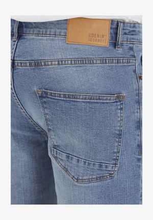 Svijetloplave traperice s stražnjim džepom, kožnom oznakom na pojasu i kontrastnim šavovima.