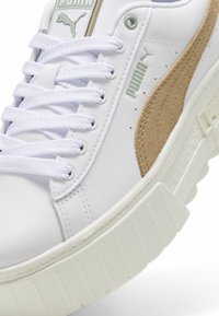 Vita lädersneakers med beige mockadetaljer, texturerad gummisula och bomullsn offset. Har en logotyp nära tungan och på sidan.