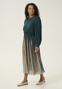 Long pleated dress with a teal top and beige striped skirt; features a cinched waist and flowing, lightweight fabric, paired with beige flats.