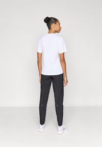 Λευκό μπλουζάκι με κοντά μανίκια και στρογγυλή λαιμόκοψη, συνδυασμένο με μαύρο στενό παντελόνι με φερμουάρ στους αστραγάλους και λευκές λεπτομέρειες.