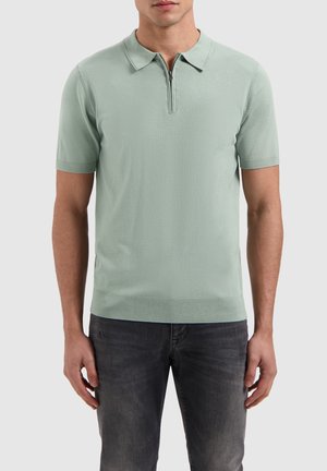 Light green short-sleeve polo shirt with a collar and a zipper, made from a textured fabric, paired with dark jeans.