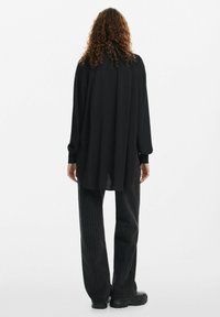 Maglietta nera a maniche lunghe con vestibilità rilassata, tessuto morbido, orlo dritto e dettaglio sulla parte posteriore, abbinata a pantaloni neri a righe sottili e scarpe chunky.
