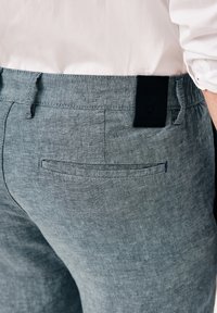 Light gray linen pants featuring a relaxed fit, elastic waistband, and rear pocket with navy stitching. Black brand tag on the waistband.