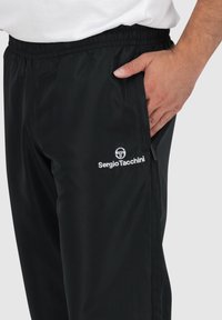 Schwarze Sporthose mit elastischem Bund, Seitentaschen und einem weißen gestickten Logo auf dem linken Oberschenkel. Glattes, leichtes Material.