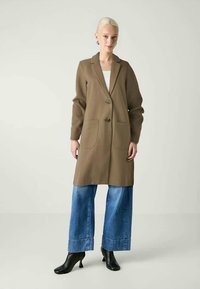 Brown long coat with two front pockets and buttons, paired with wide-leg blue denim jeans and black ankle boots. Smooth texture.