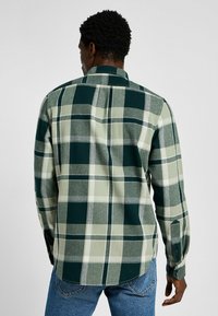 Groen en grijs geruite langwerpige shirt met lange mouwen in een zachte stof; voorzien van een button-down kraag, enkele knopmanchet en een gebogen zoomdesign.