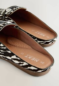 Schwarz-weiße Zebra-Muster-Sandalen mit einem braunen strukturierten Fußbett und silbernem Schnallen-Detail. Weiche Innenauskleidung für Komfort.