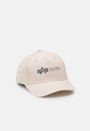 Căciulă de baseball din material bej, având un logo negru "ALPHA INDUSTRIES" și un design cu o vizieră curbată și accente cusute.