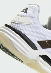 Weißer Sportschuh mit Netz-Obermaterial, schwarzen Akzenten und strukturiertem Zwischensohlenteil. Verfügt über ein auffälliges Logo und eine glatte Gummisohle.