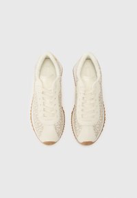Cremefarvede sneakers med mønstrede sider, snørebånd, polstret krave og gummisåler. Stofstruktur med glat og blød finish.