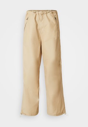 Beige, kerge püksid, millel on nööriga vöökoht, külgzippide ja elastsete mansettidega. Sile tekstuur, sirge säärte disain.