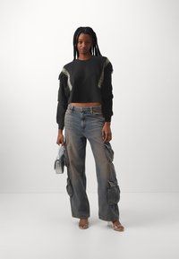 Felpa nera corta con frange; jeans cargo chiari con molte tasche; borsa argentata; tacchi trasparenti.