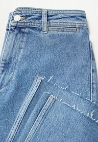 Jean en denim bleu clair plié, avec fermeture à bouton, passants de ceinture et ourlets bruts effilochés sur les jambes.