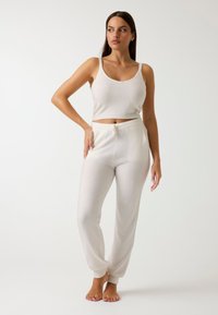 Débardeur en tricot blanc avec des bretelles réglables et pantalon taille haute assorti avec taille à cordon de serrage et poignets côtelés. Texture lisse.