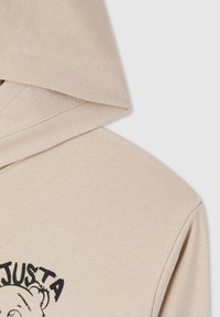 Hoodie beige con un tessuto testurizzato, cappuccio con cordino e una stampa grafica nera di un orso sul davanti.