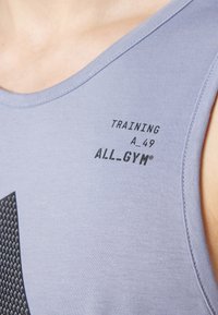 Lys lilla trenings tank top laget av glatt stoff, med trykt svart tekst: "TRAINING A 49 ALL_GYM®" og et mønster på nedre venstre side.